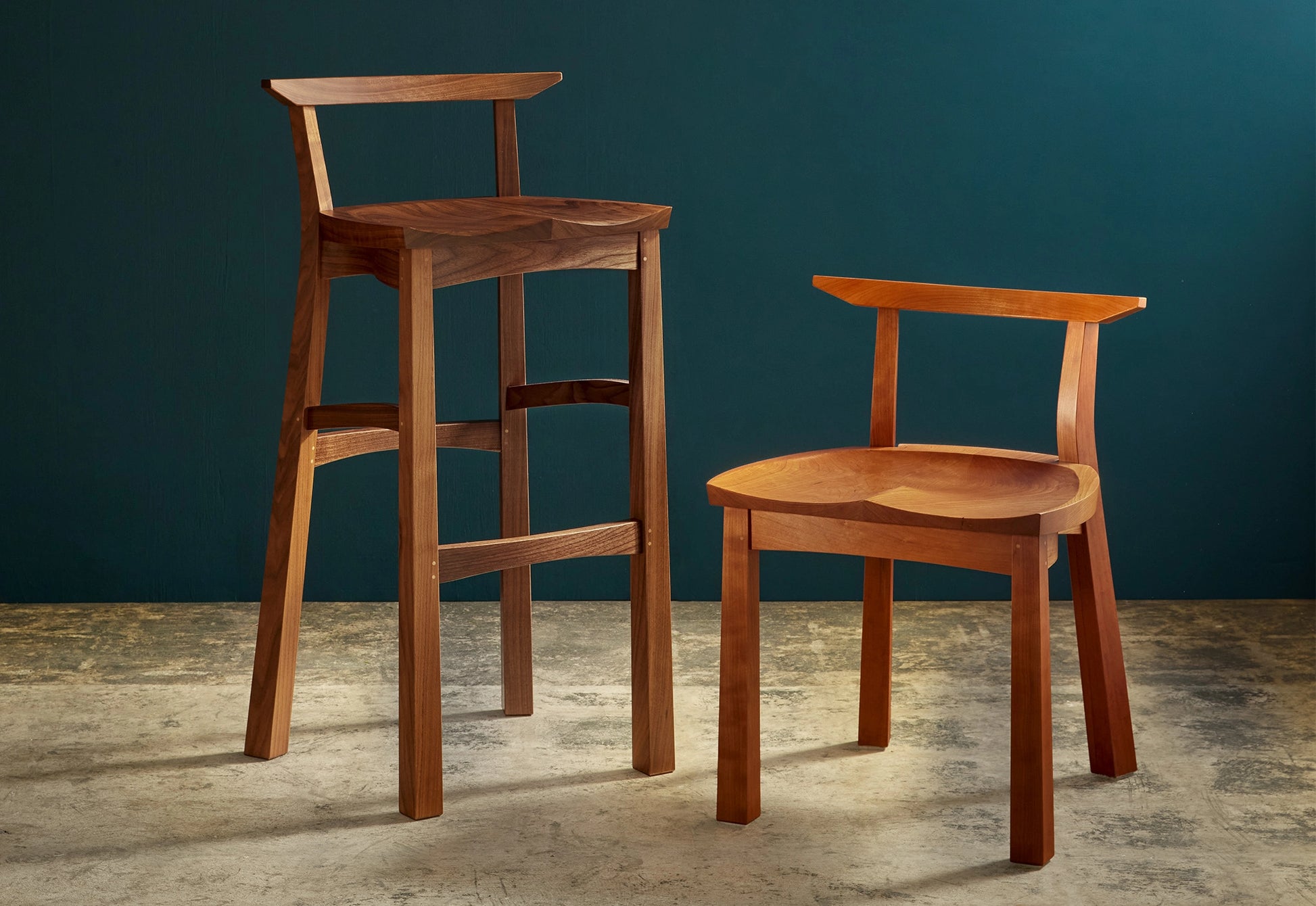 Two wooden chairs, one tall and one short, against a dark blue wall.