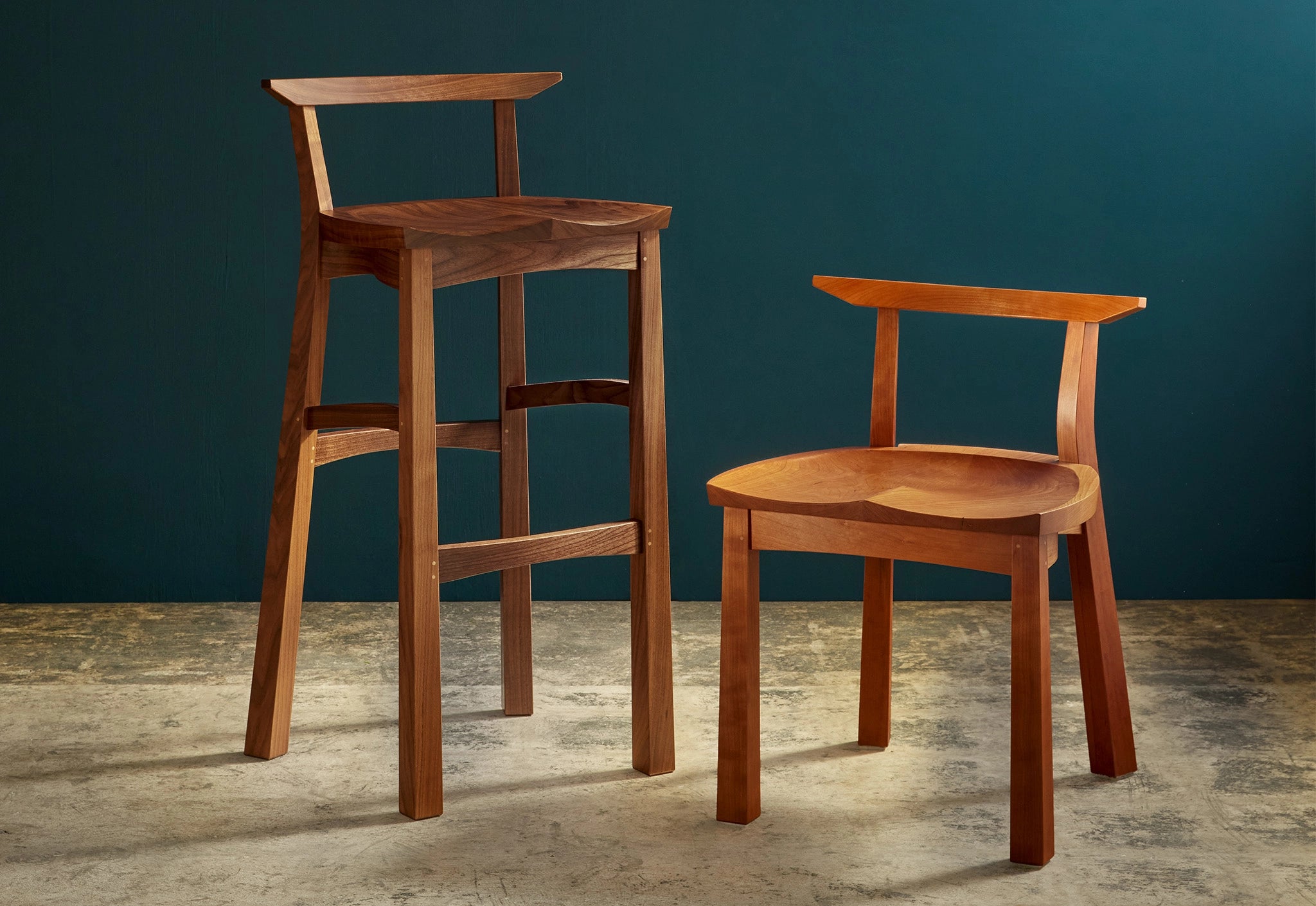 Two wooden chairs, one tall and one short, against a dark blue wall.