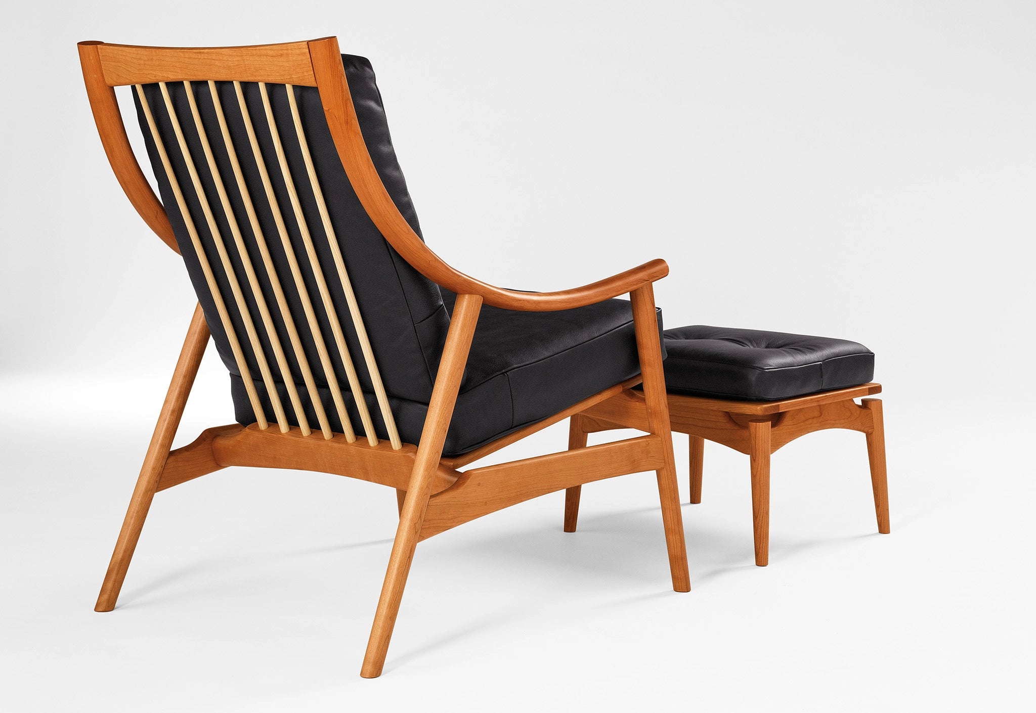 Wooden armchair with black leather seat and ottoman on a white background