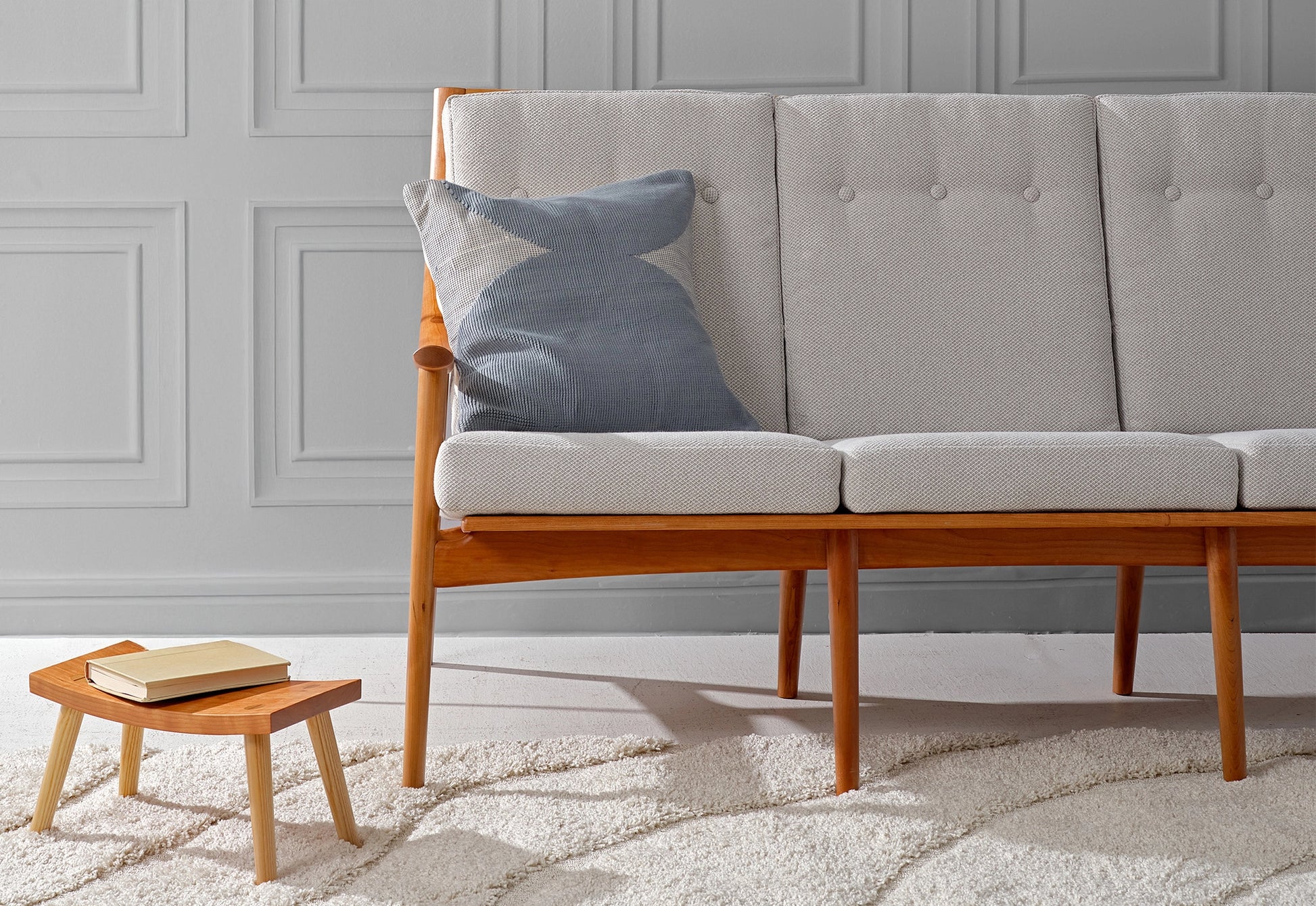 Gray sofa with wooden legs in a room with a gray wall and white rug.
