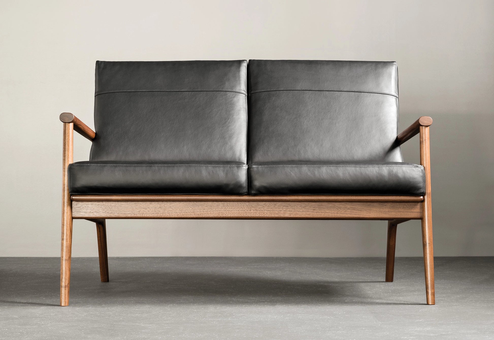 Walnut lounge chair with black leather on a gray wall.