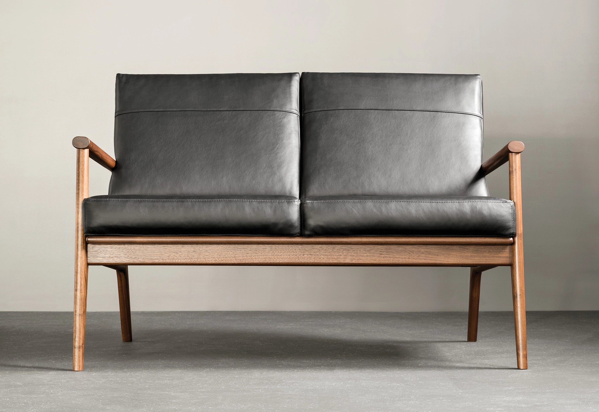 Walnut lounge chair with black leather on a gray wall.