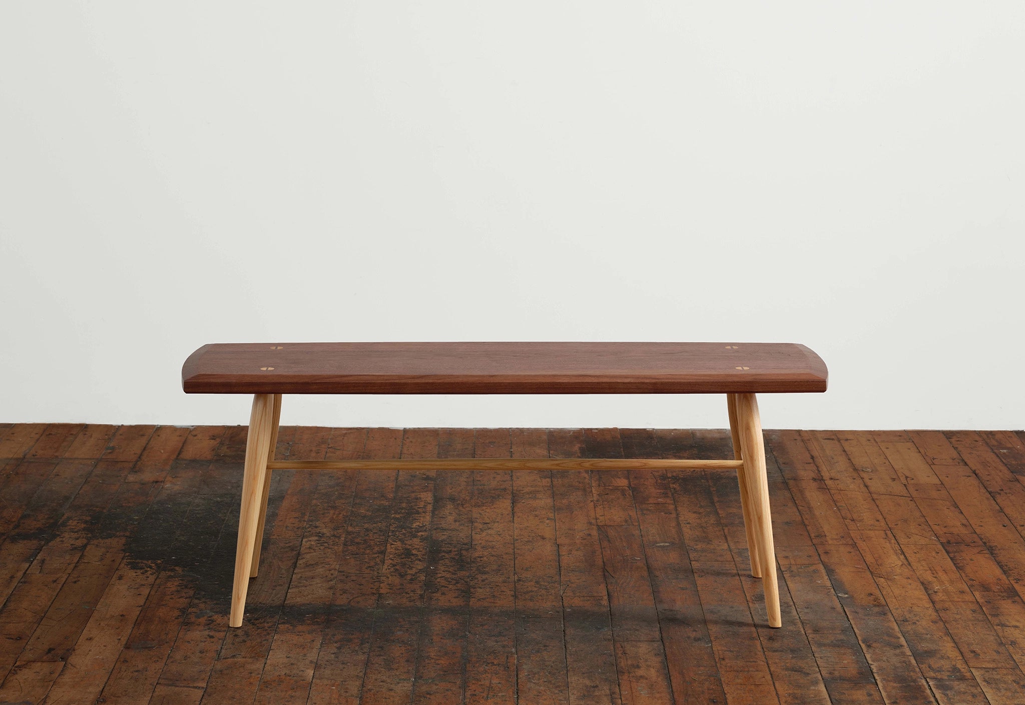 Wooden bench on a wooden floor with a white wall background