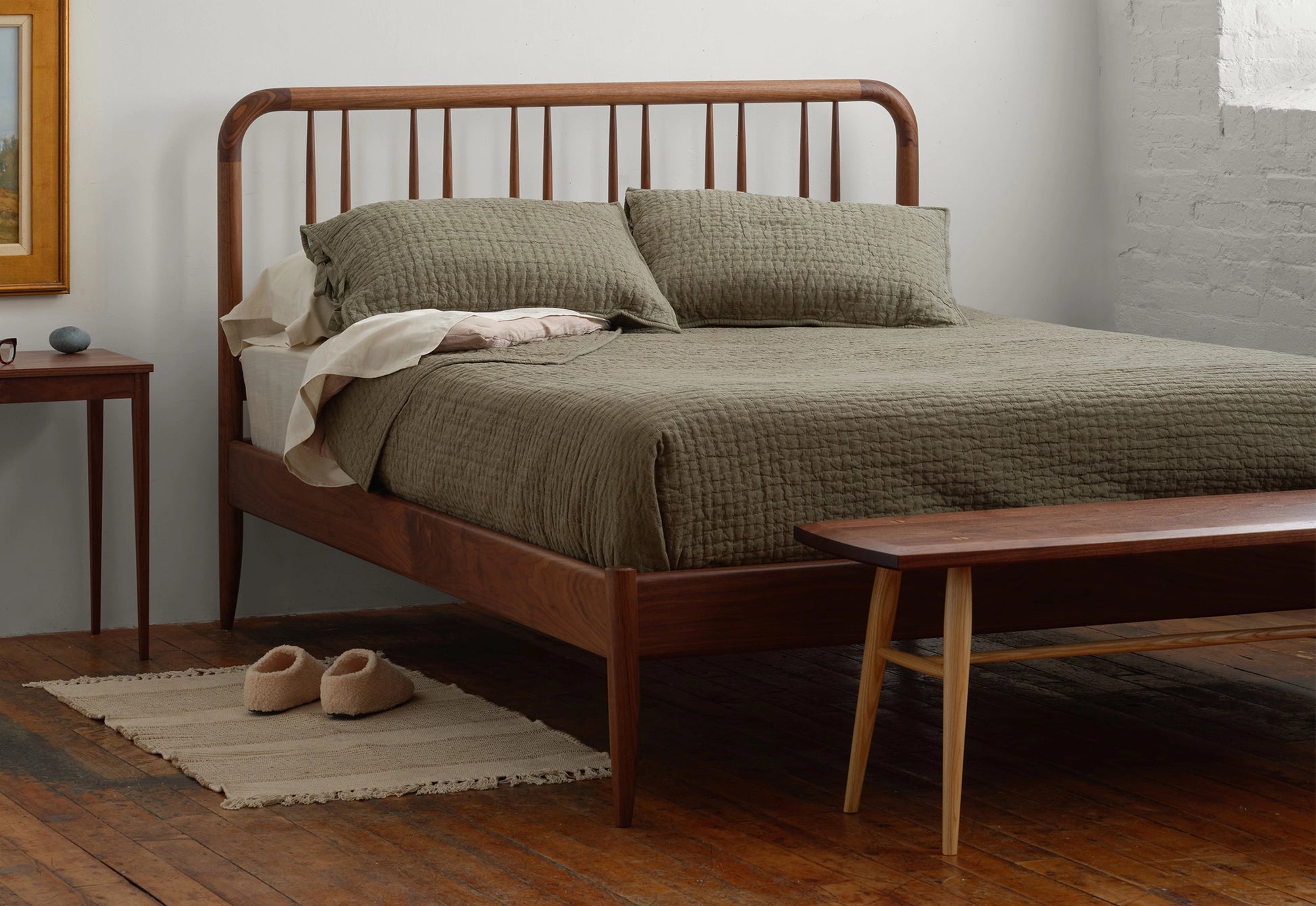 Bedroom with wooden bed frame, green bedding, and wooden bench.