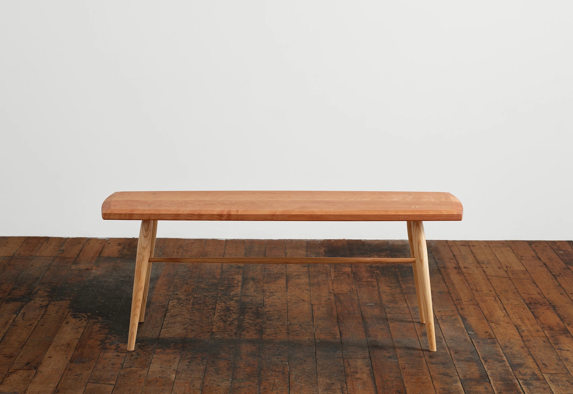 Wooden bench on a wooden floor with a white wall background