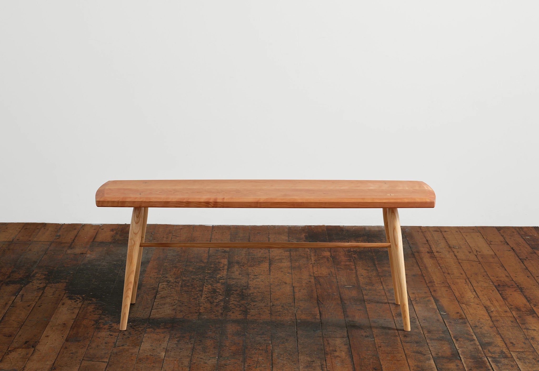 Wooden bench on a wooden floor with a white wall background
