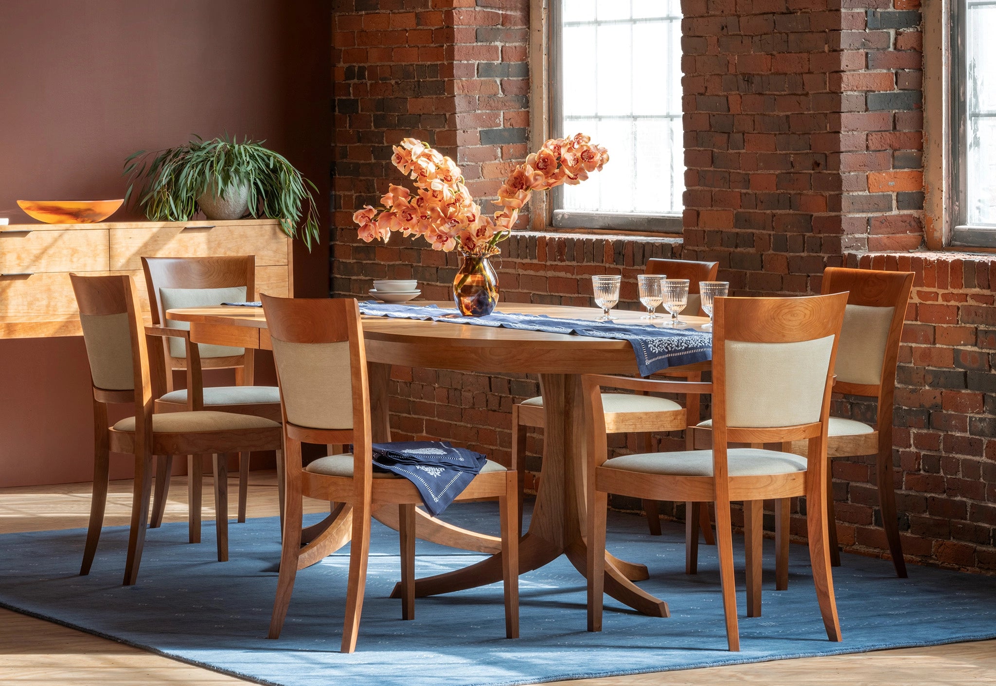 Dining room with wooden table and chairs in front of a brick wall.