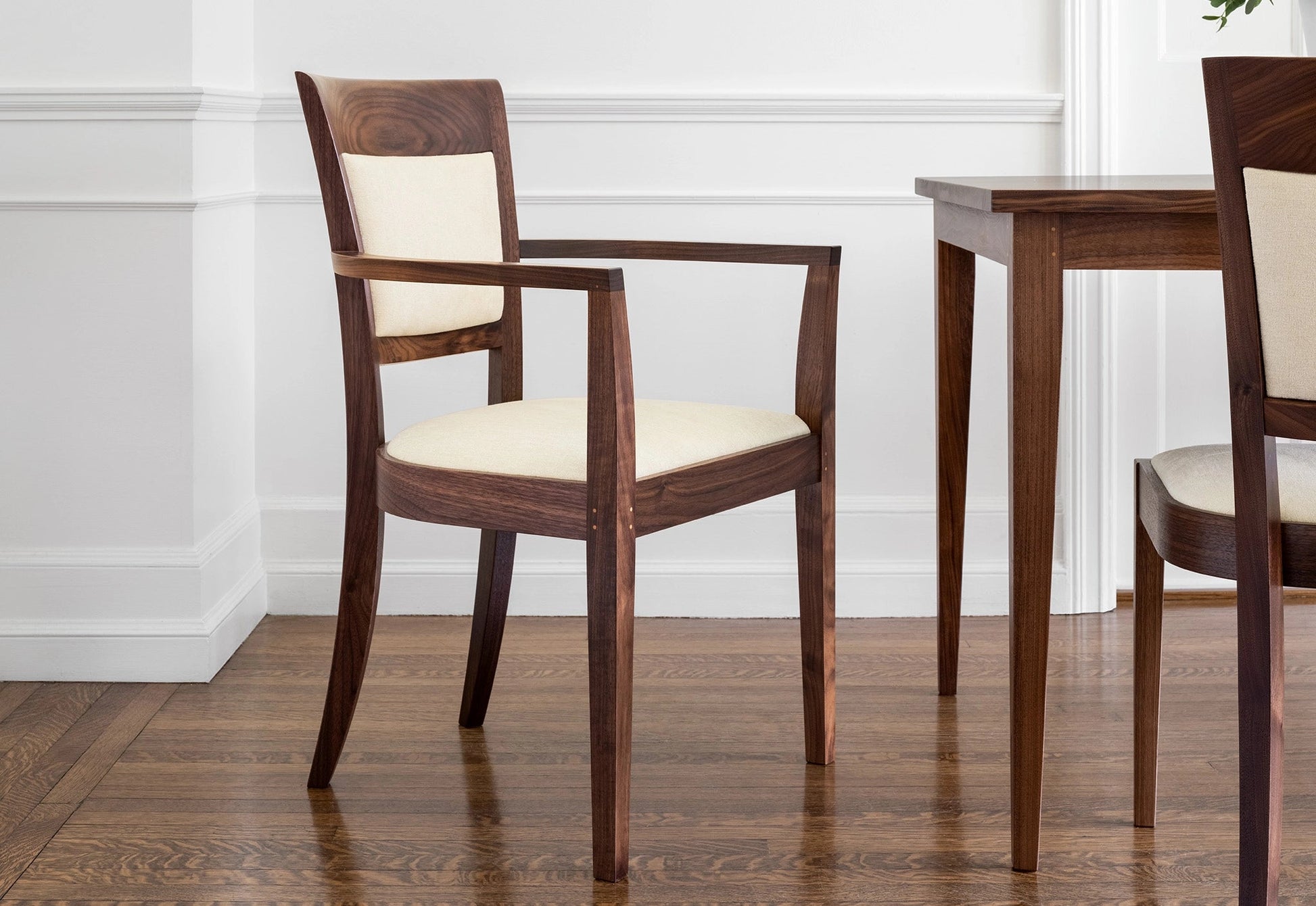 Wooden chairs with white cushions on a wooden floor against a white wall.