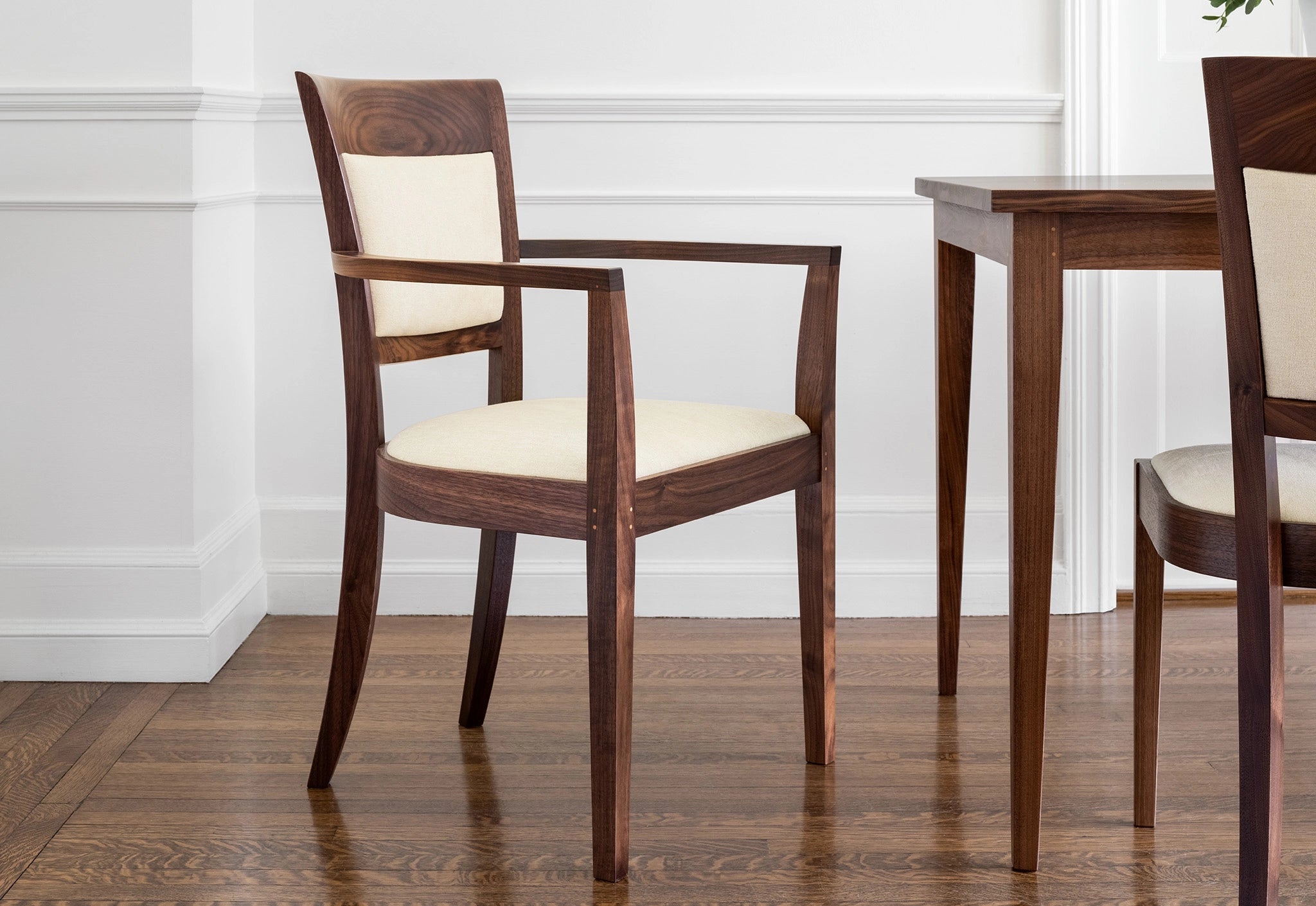 Wooden chairs with white cushions on a wooden floor against a white wall.
