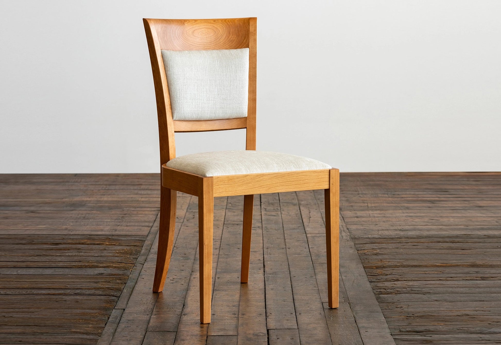 Wooden chair with a white cushion on a wooden floor.