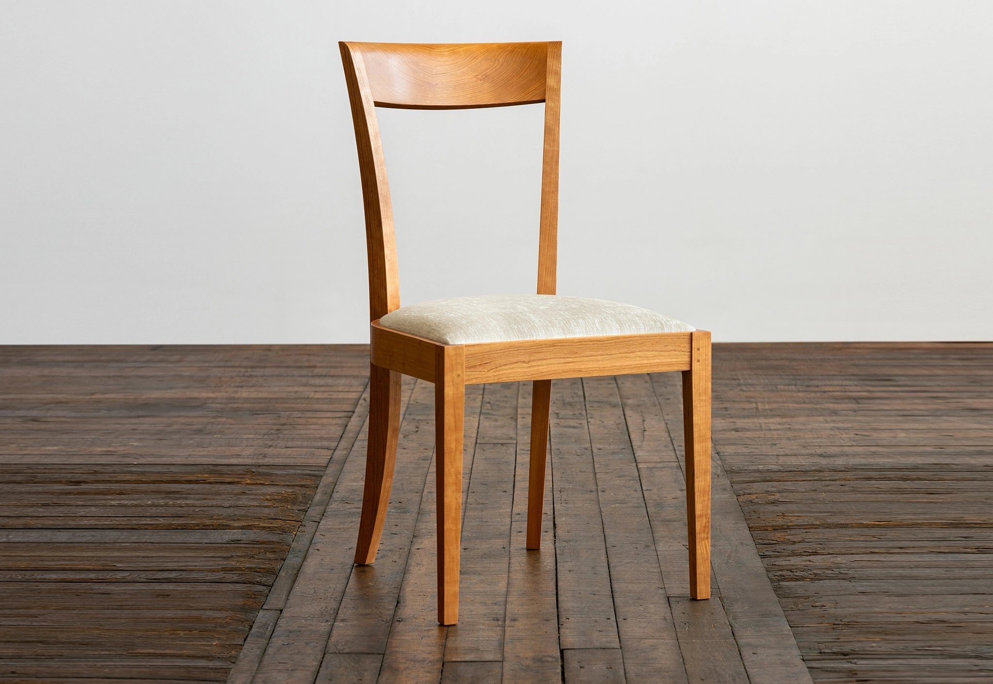Wooden chair with a white cushion on a wooden floor.