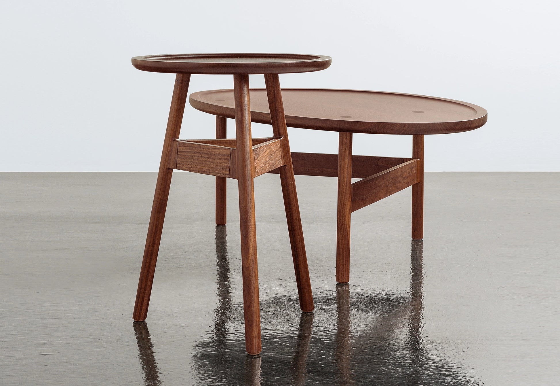 Two wooden side tables on a reflective surface with a light gray background