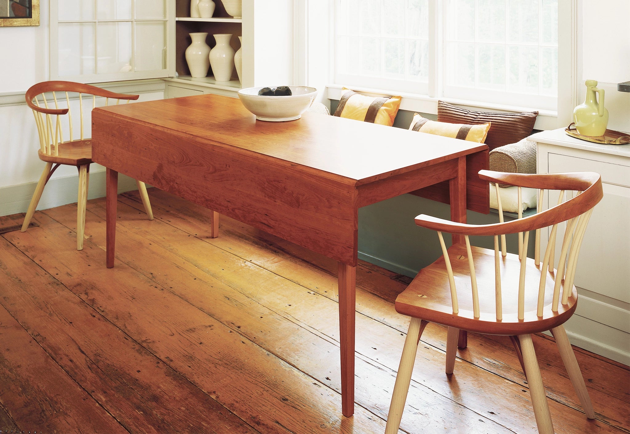 Wooden dining table with chairs in a room with white walls and a window.