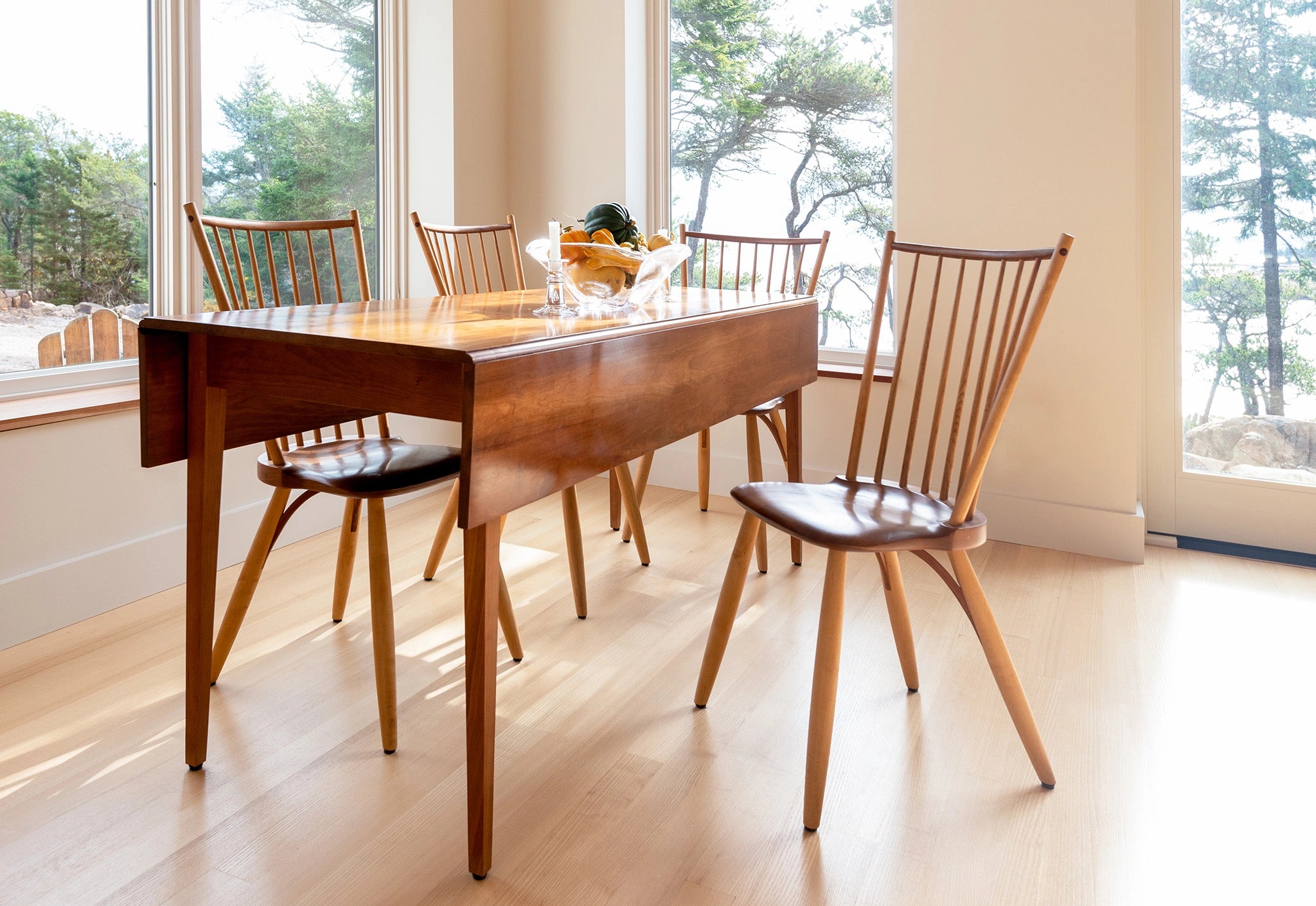 Wooden dining table with chairs in a bright room with large windows.