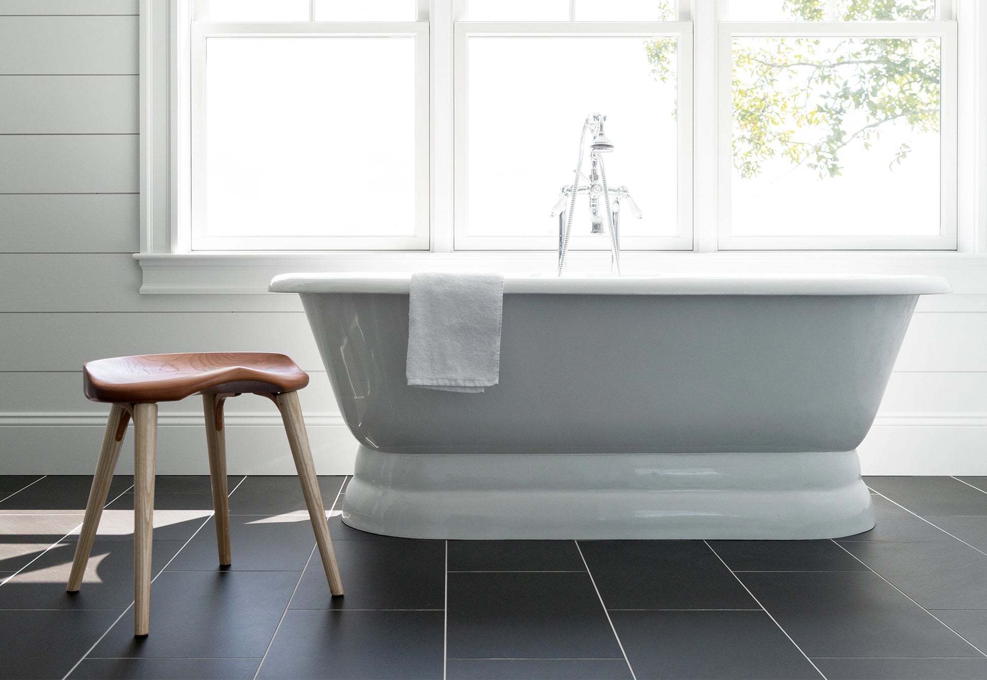 White freestanding bathtub in a bathroom with a wooden stool and towel.