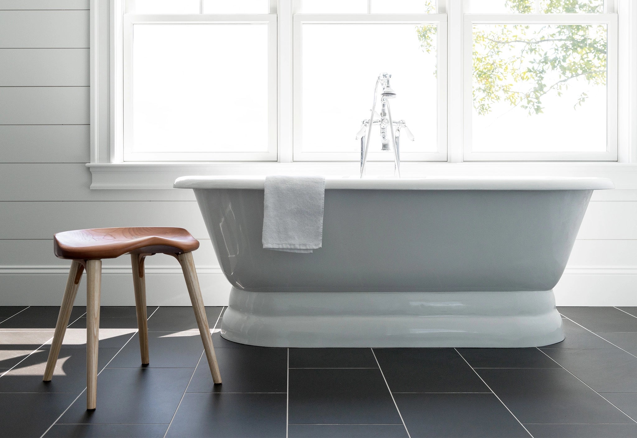 White freestanding bathtub in a bathroom with a wooden stool and towel.