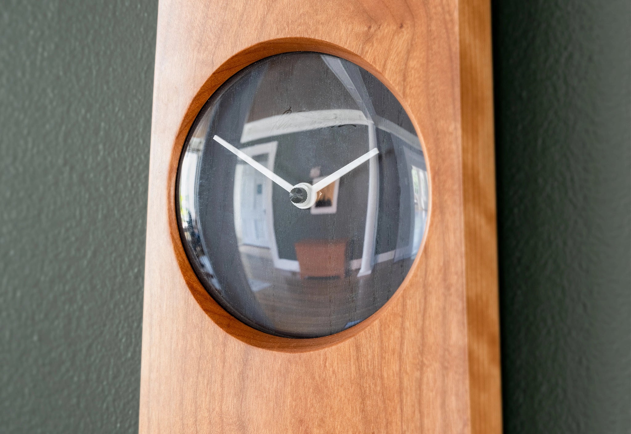 Wooden wall clock with a round glass face on a dark gray wall.