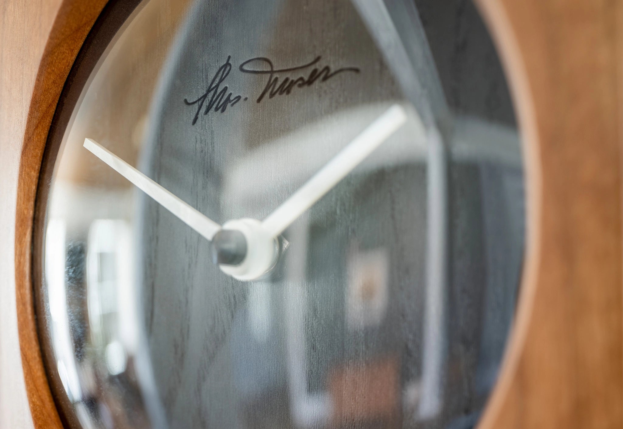 Wooden clock with a signature on the glass face, blurred background