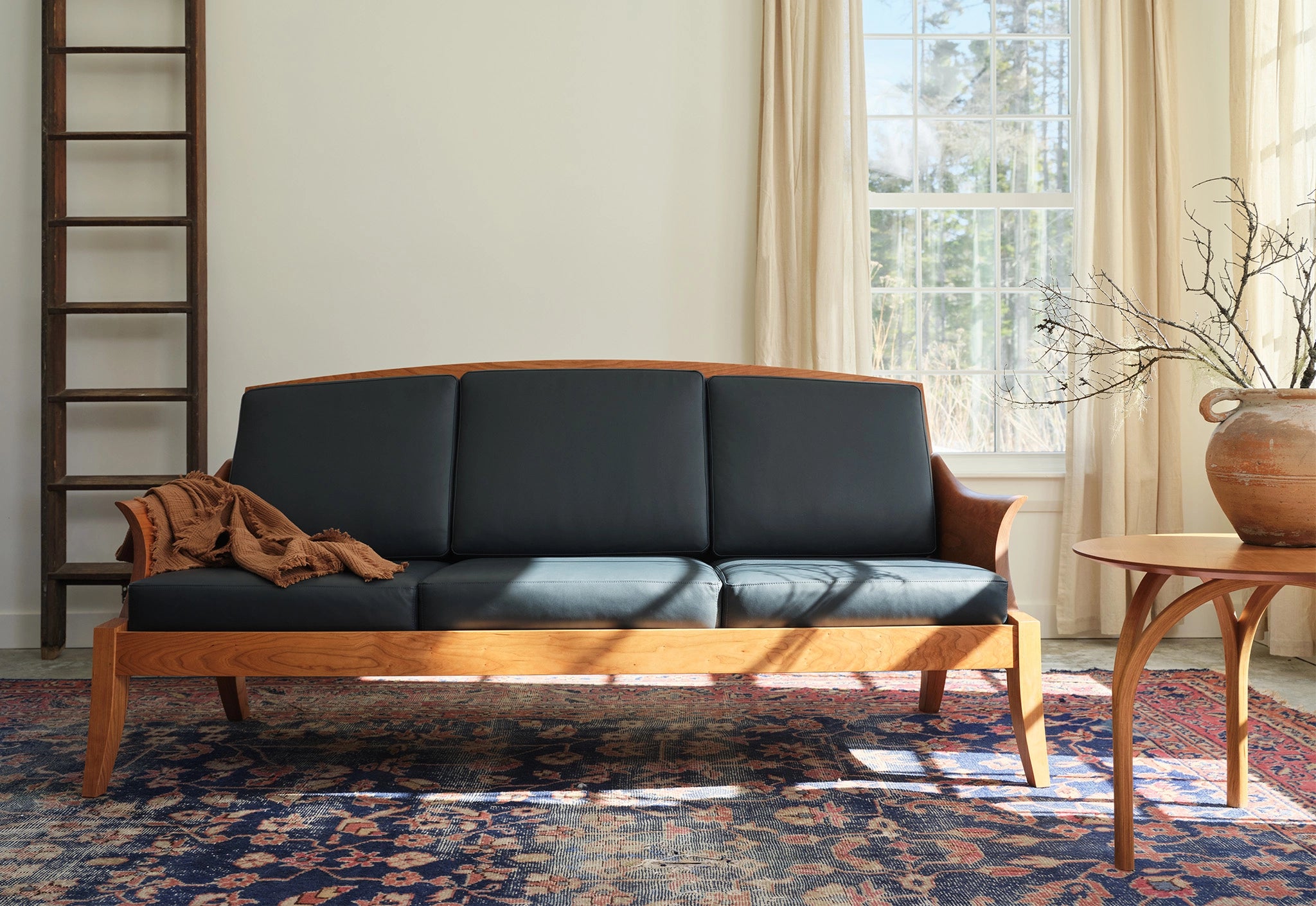 Wooden sofa with dark cushions in a room with a window and decorative rug.