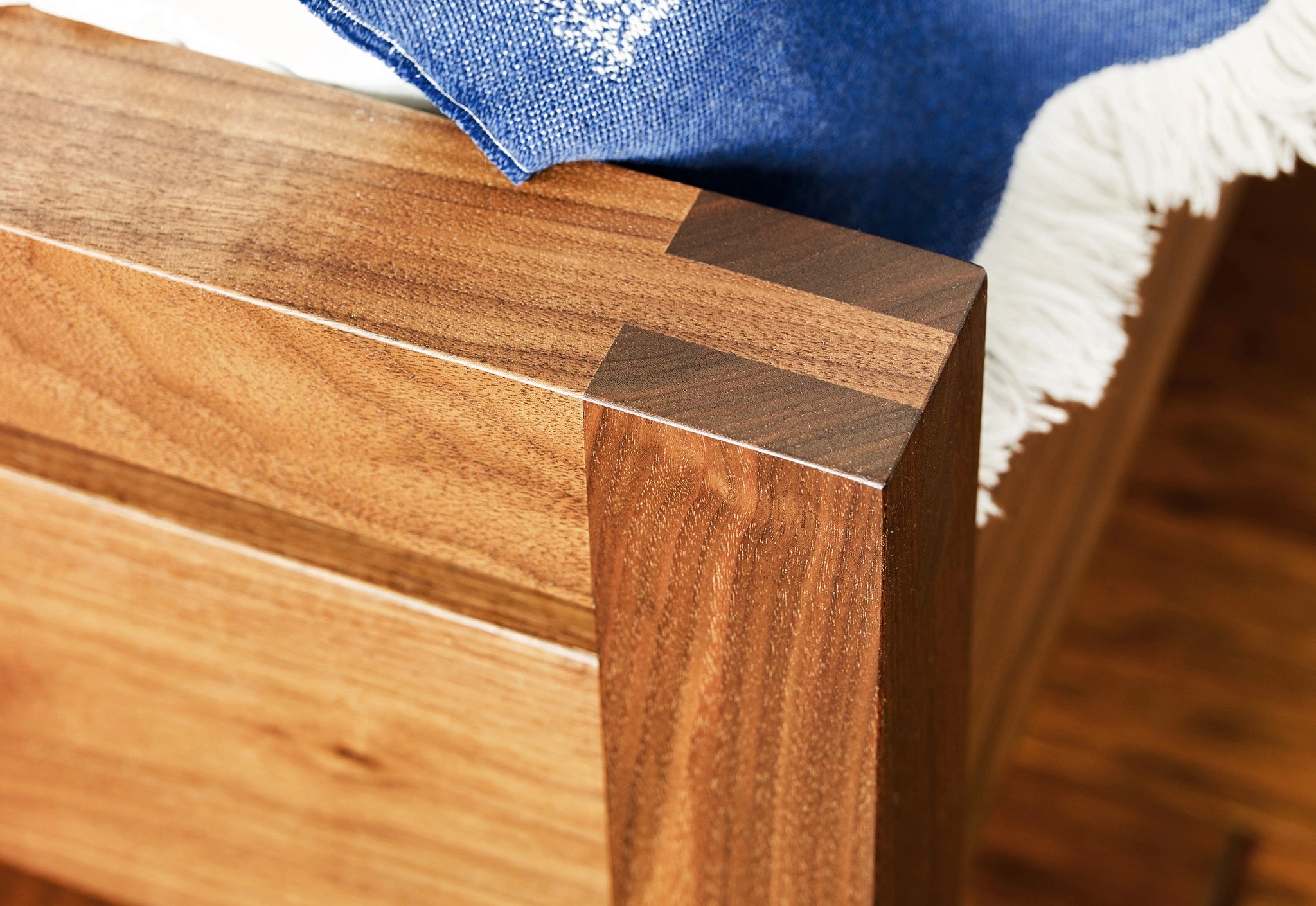 Close-up of a wooden bench corner with a white blanket in the background.