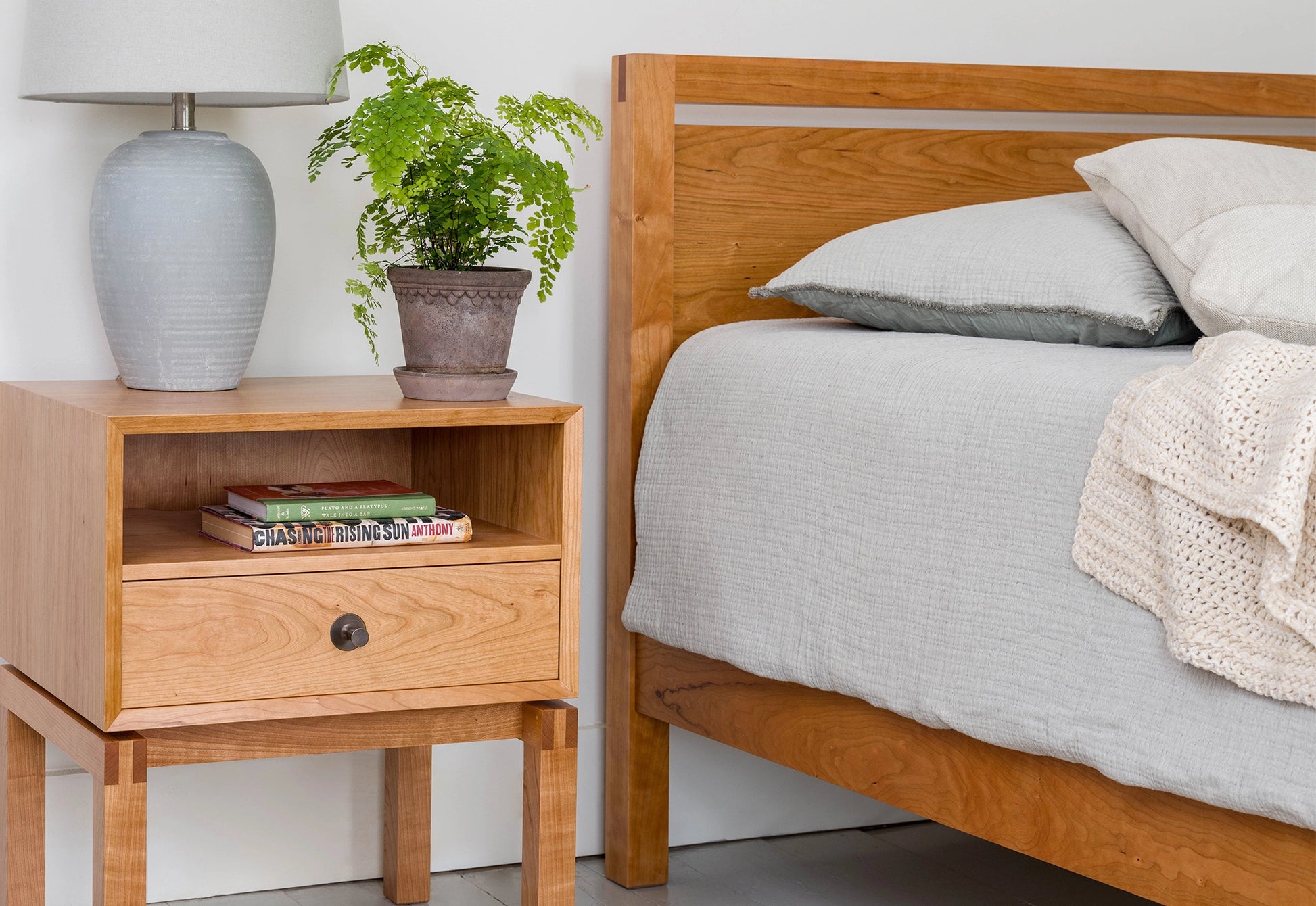 Cherry Bed and Side table on a white wall with lightly colored bedding.