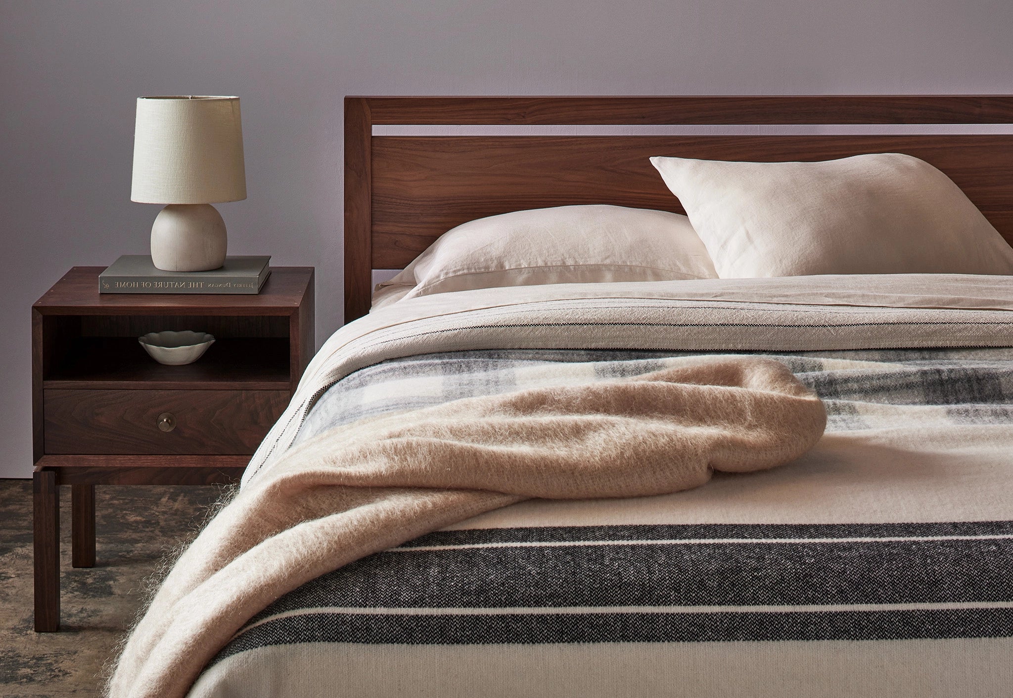 walnut wooden bed with soft bedding and a lamp for accent.