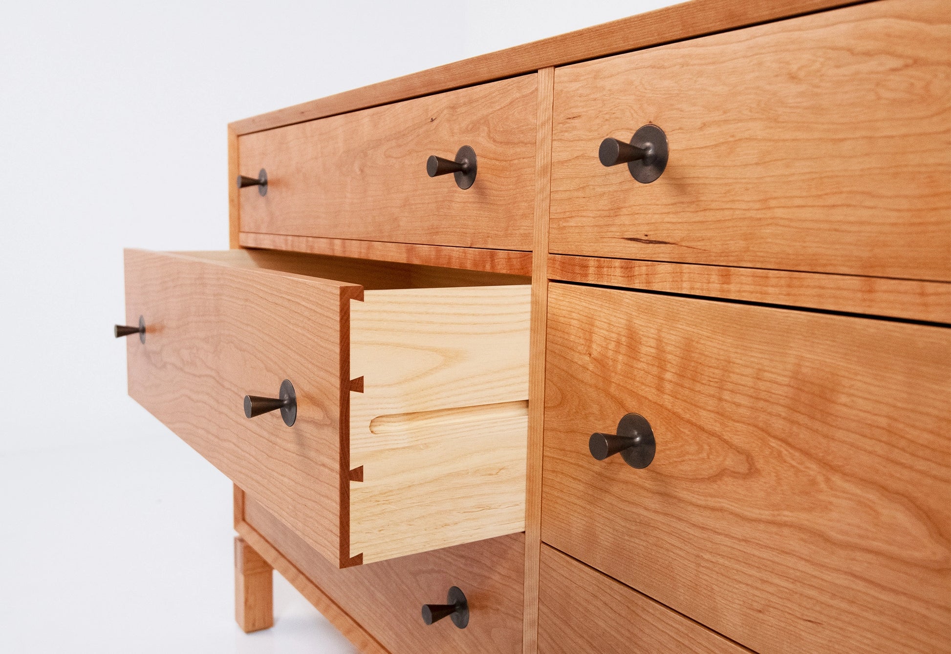 Wooden dresser with multiple drawers and black handles on a white background