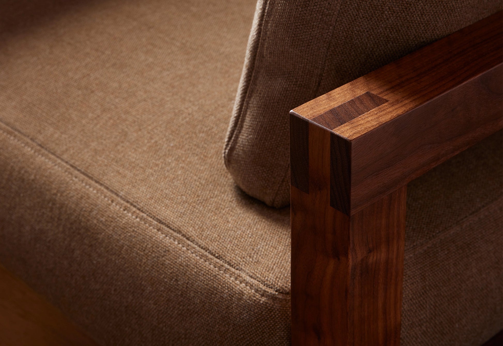 Detail of a wooden-framed sofa with brown upholstery on a white background.