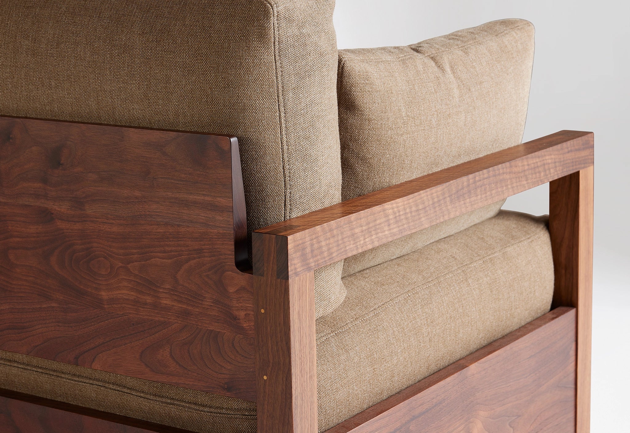 Detail of a wooden-framed sofa with brown upholstery on a white background.