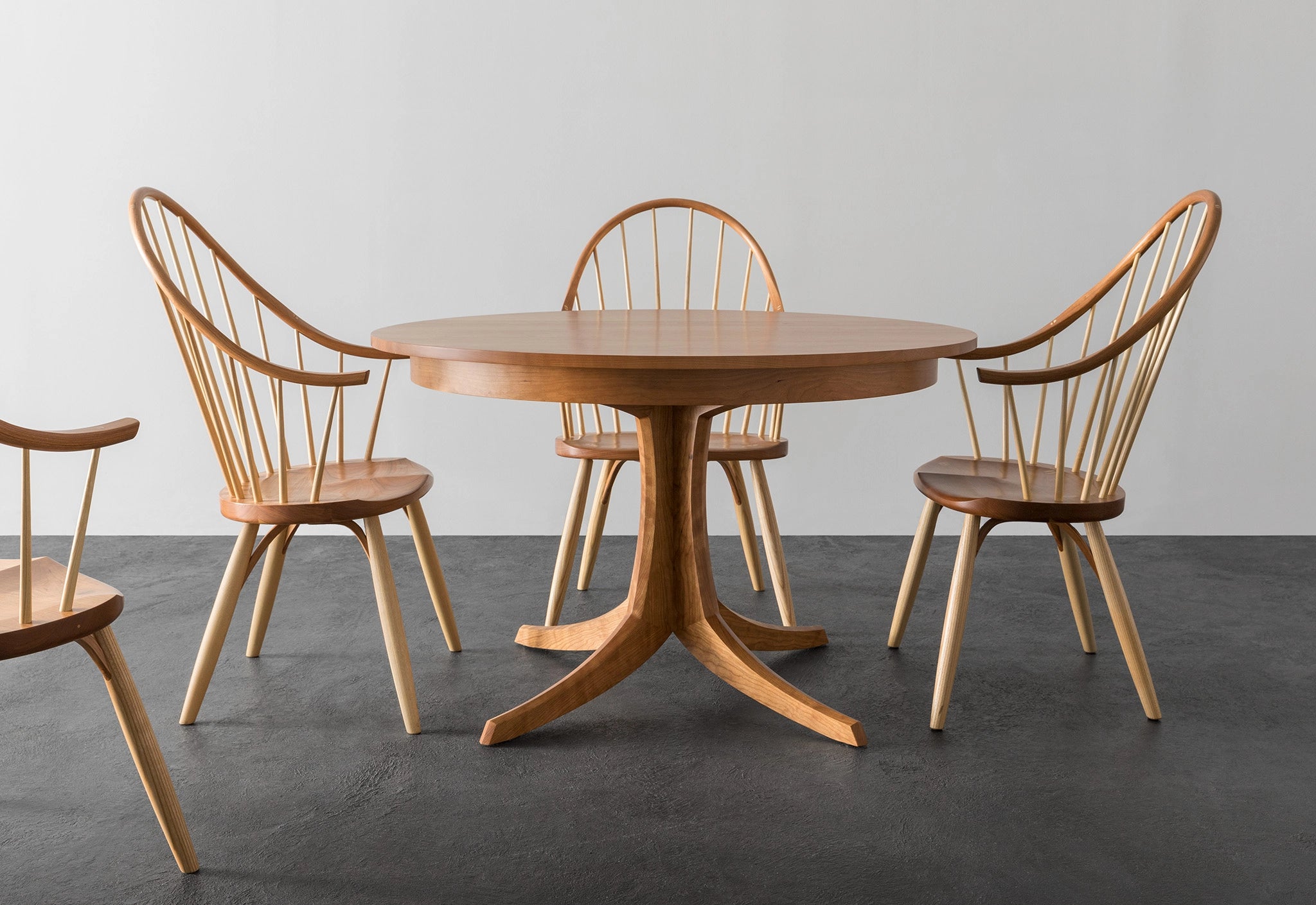 Wooden dining table with four matching chairs on a gray floor against a white wall.