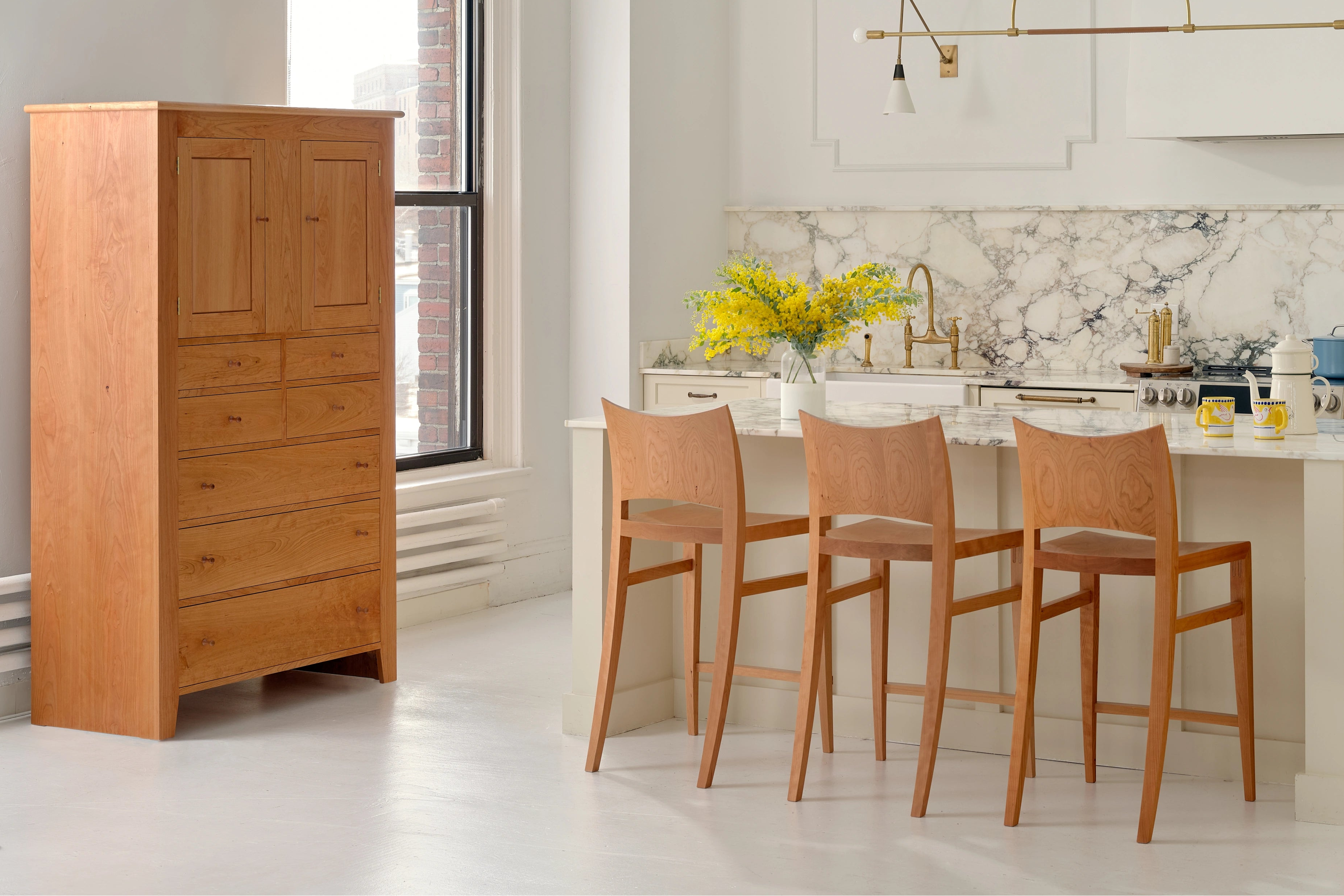 Modern kitchen with marble countertops, wooden bar stools, and a tall wooden cabinet.