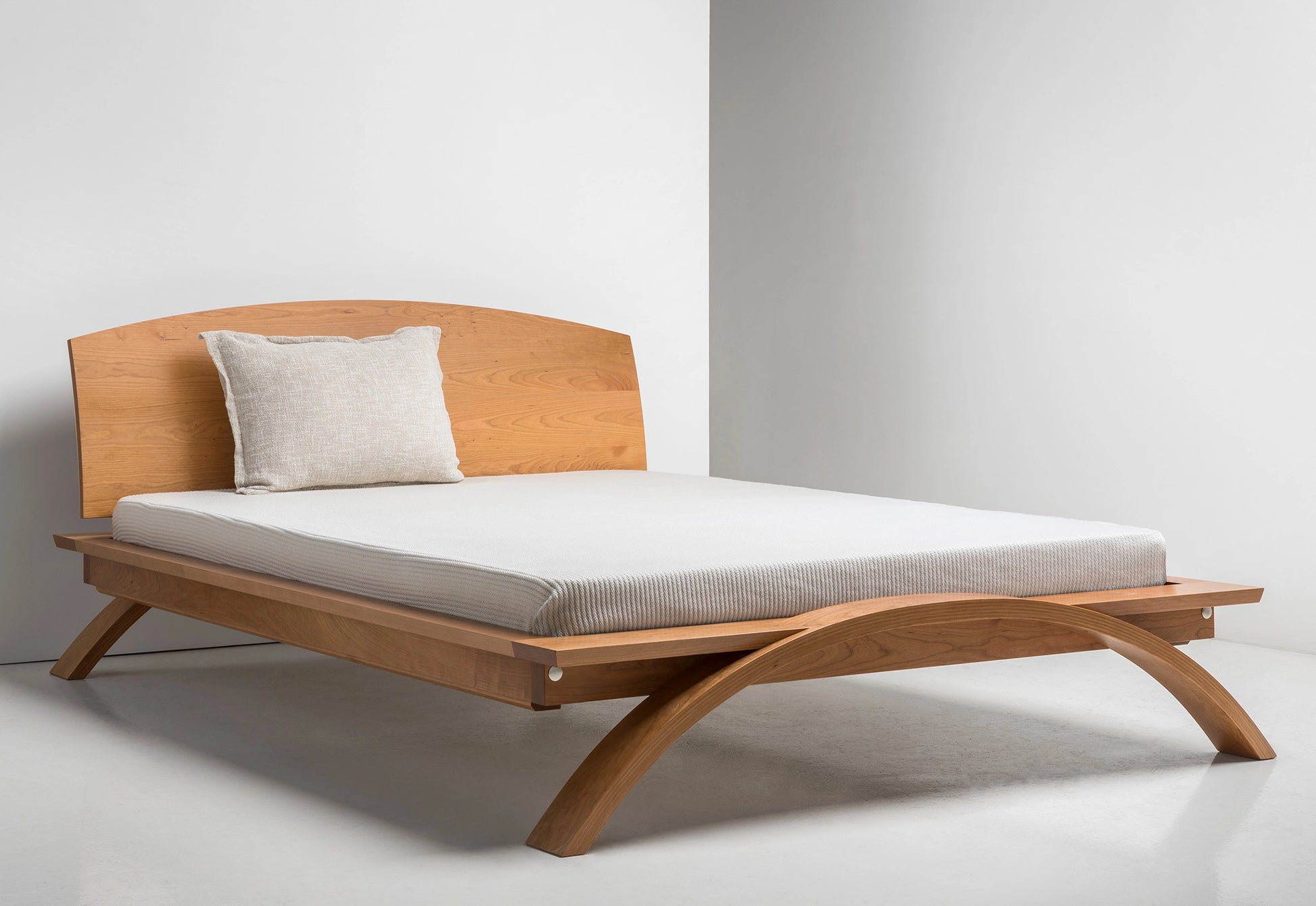 Wooden bed with a white mattress and pillow against a plain background