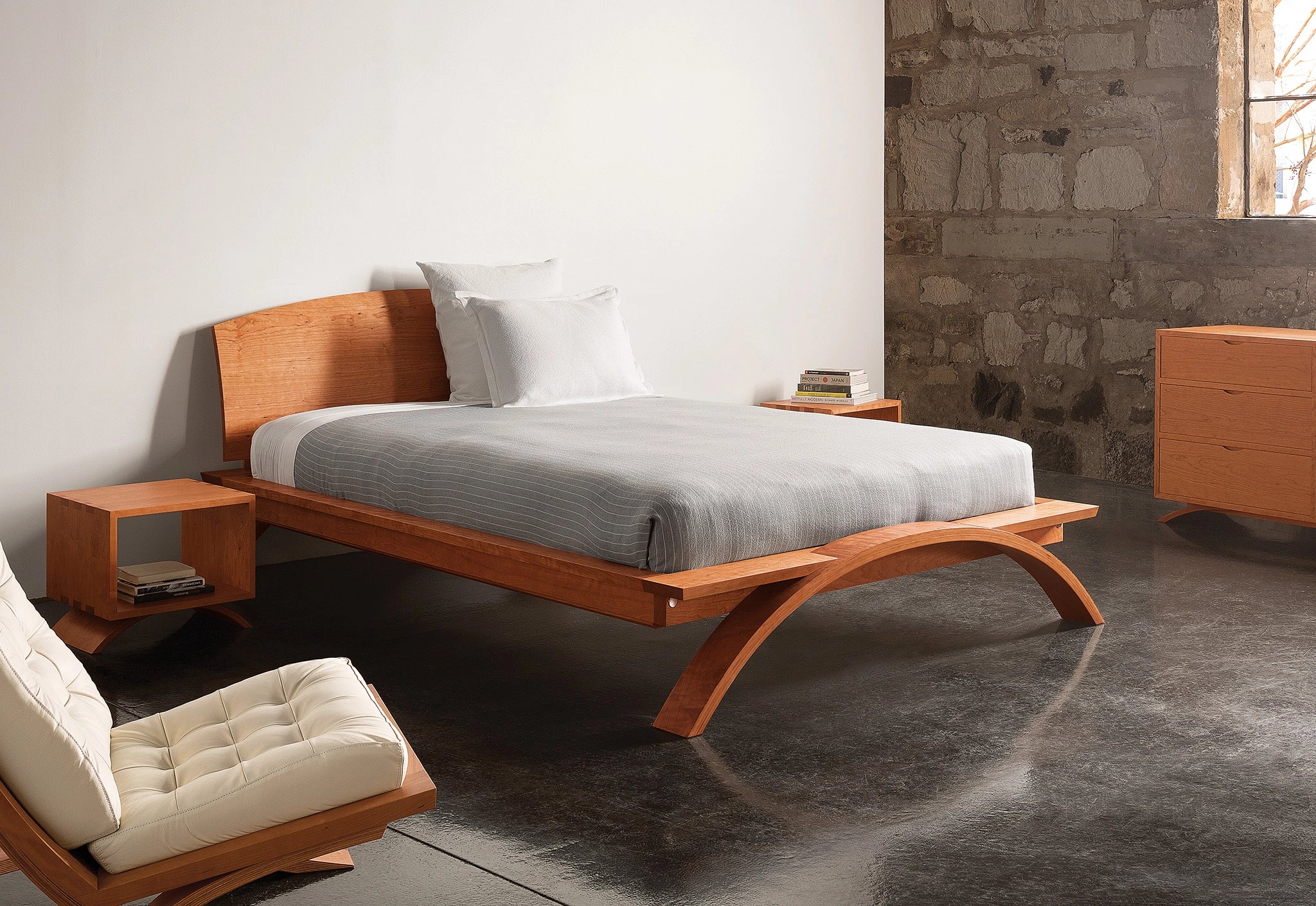 Wooden bed with gray bedding in a room with stone walls and wooden furniture.
