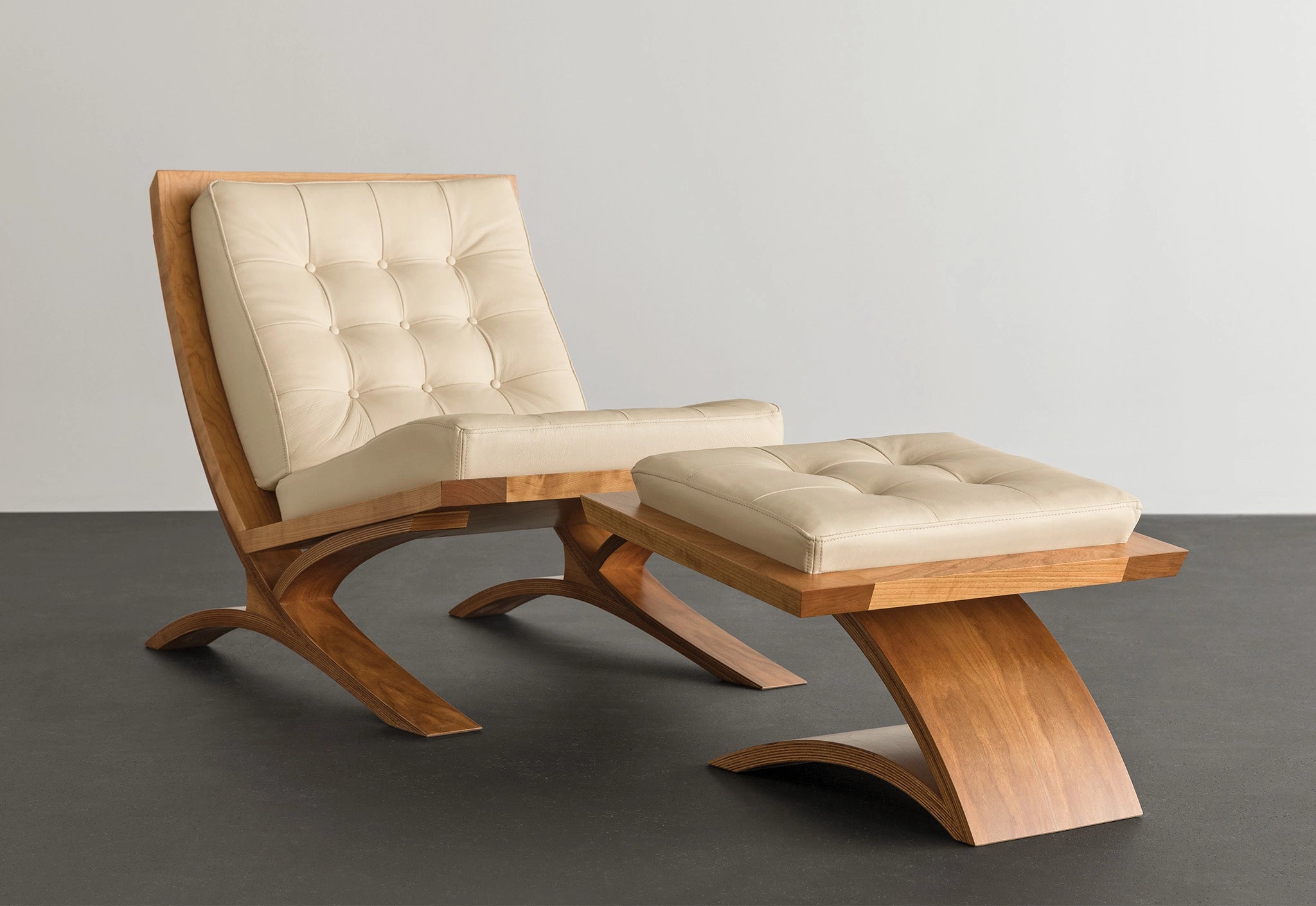 Wooden lounge chair with cream leather on a concrete floor.