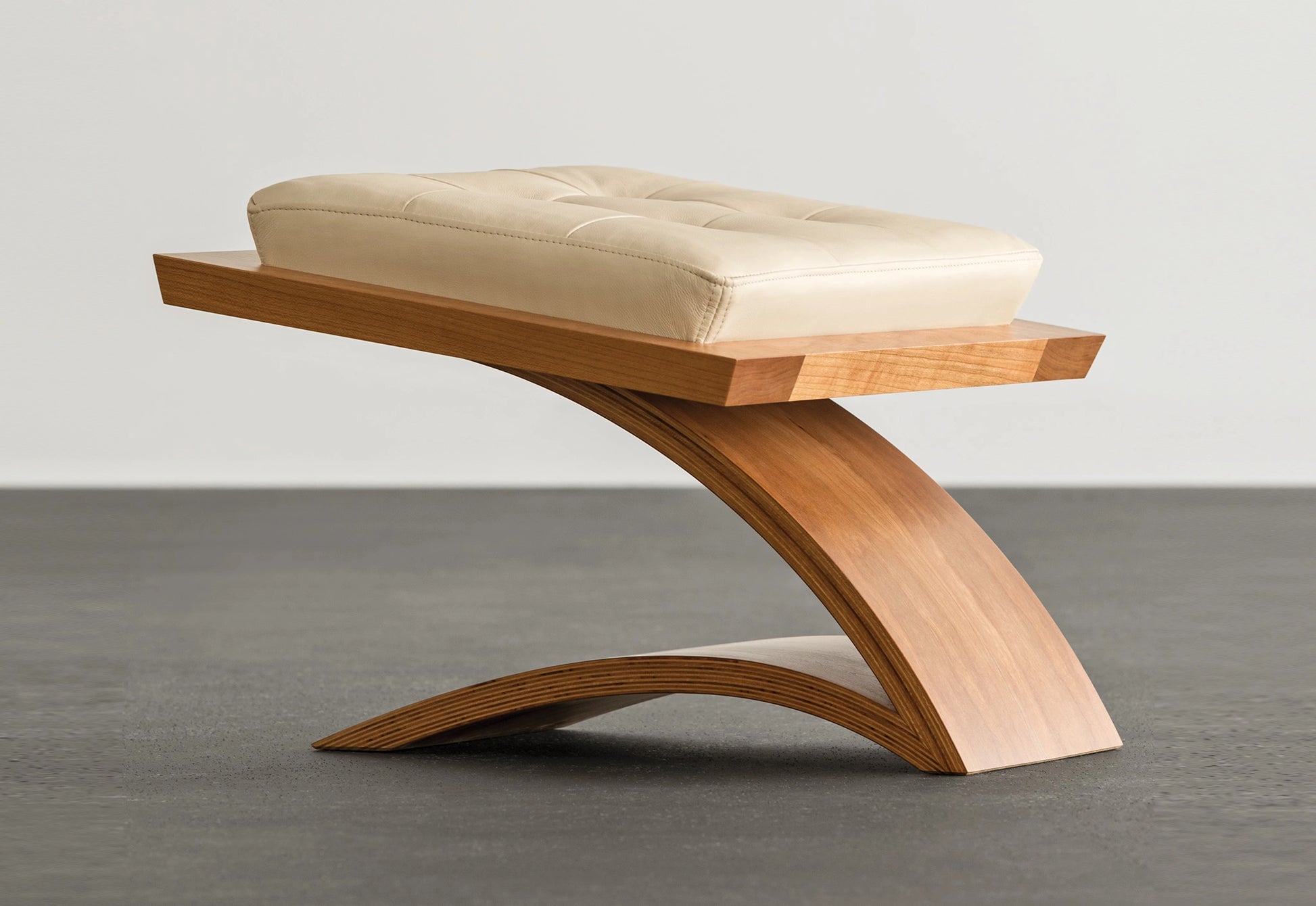 Wooden ottoman with cream leather on a concrete floor.