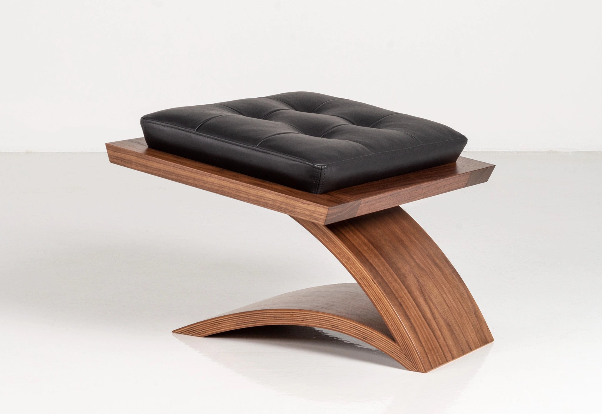 Wooden ottoman with black leather on a white background.