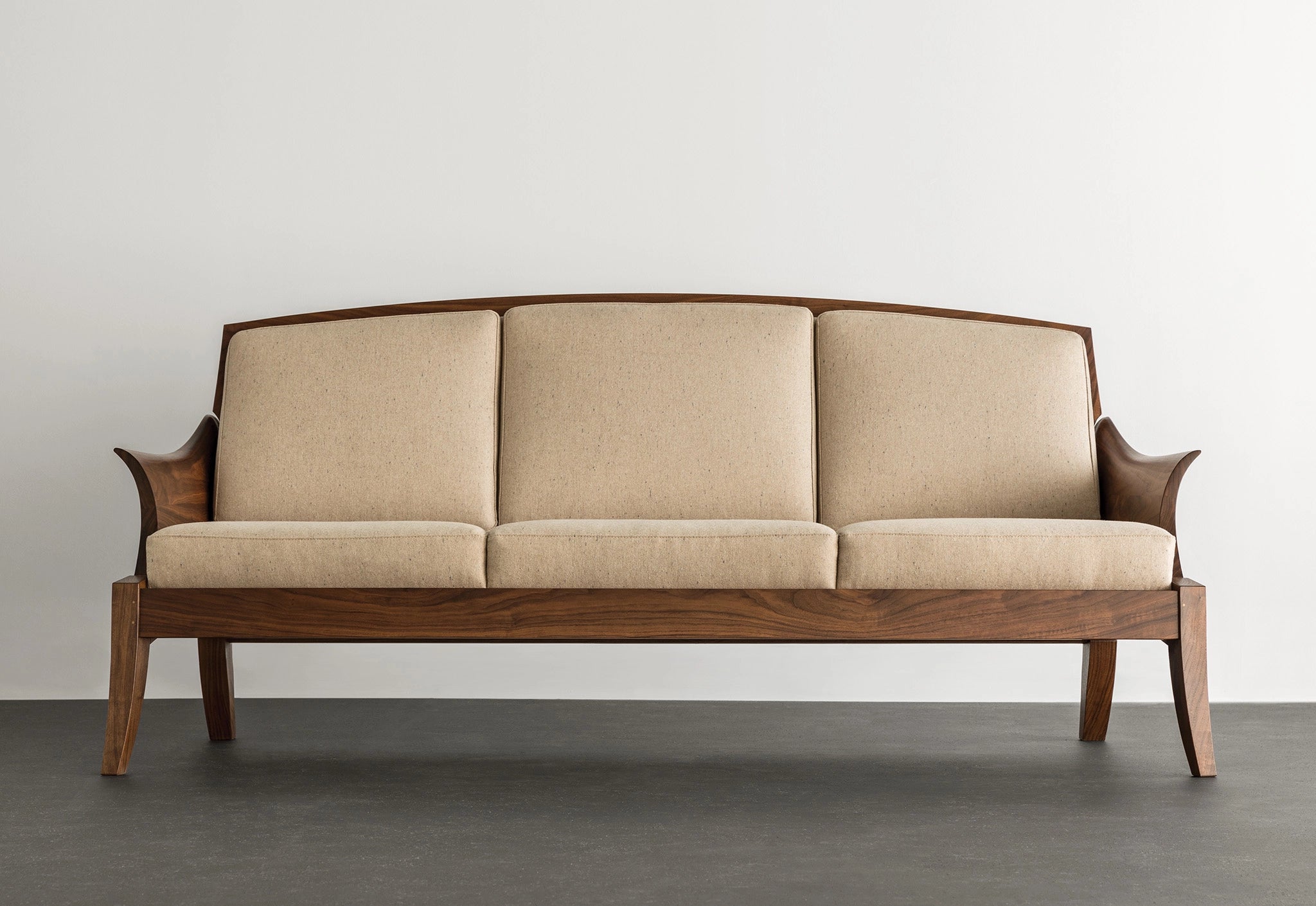 Beige sofa with wooden frame on a gray floor and white wall