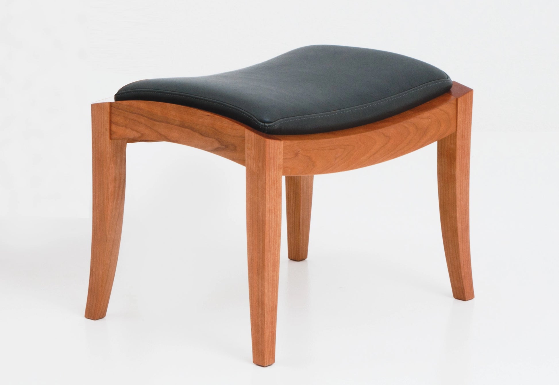 Cherry wood ottoman with black leather on a white background.