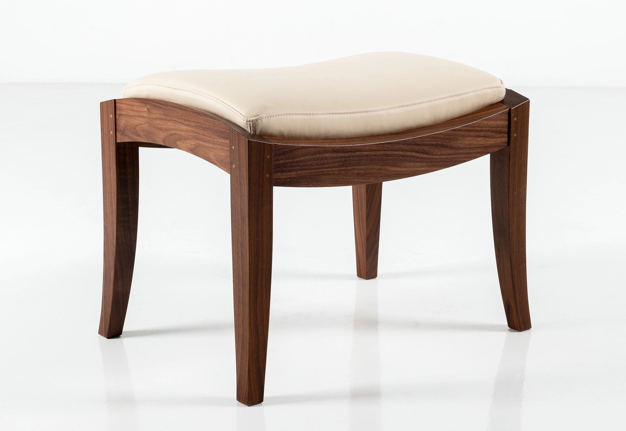 Walnut wood ottoman with cream leather on a white background.