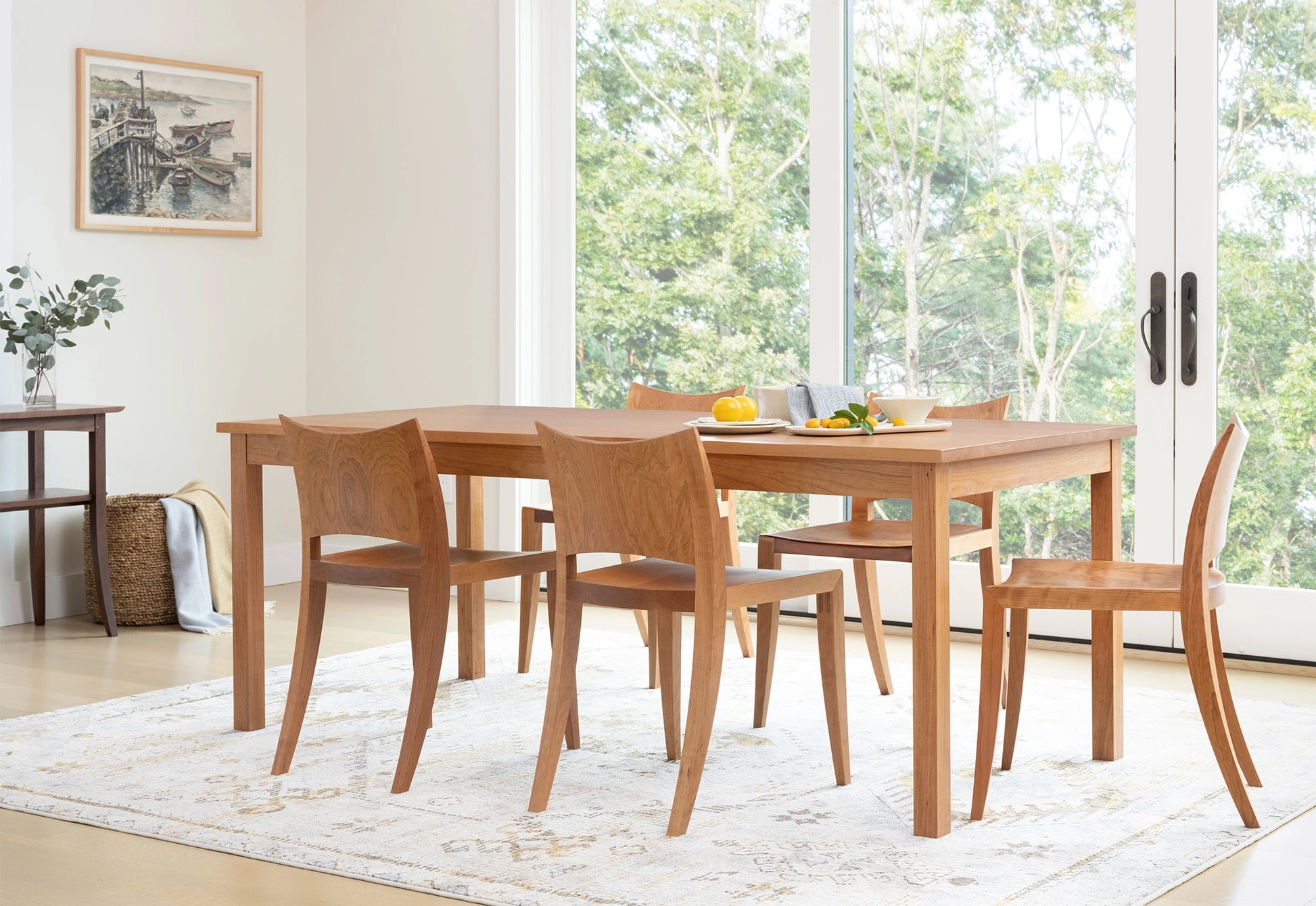 Wooden dining table with chairs in a bright room with large windows.