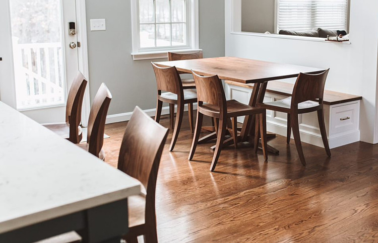 Open dining room with breakfast nook in background with Edo Trestle Table in walnut and auburn chairs in walnut with built-in bench. Auburn stools in foreground at kitchen island
