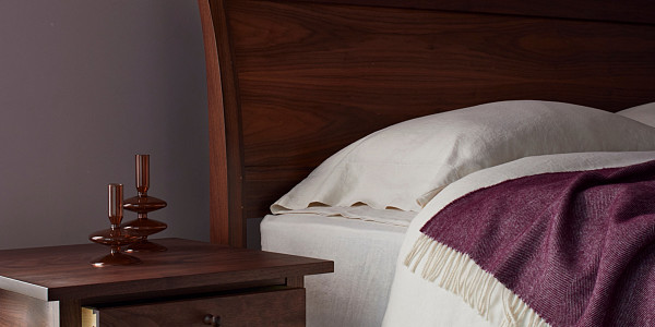 Walnut headboard of Sleigh Bed and top of walnut side table, Bed with white linens and eggplant colored throw blanket