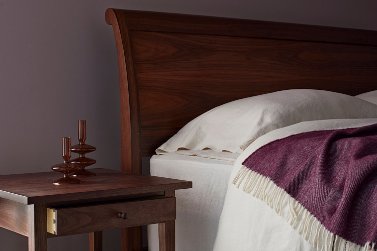 Walnut headboard of Sleigh Bed and top of walnut side table, Bed with white linens and eggplant colored throw blanket