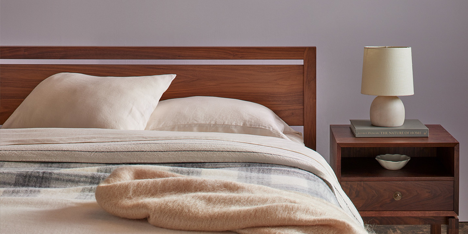 Walnut bed with woolen linens and walnut side table with brass knobs, book and white lamp