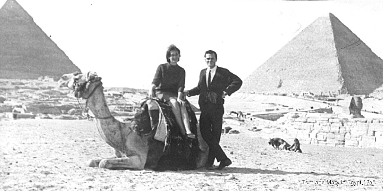 Tom and Mary Moser in Egypt in 1965 with pyramids behind them. Mary is sitting on a camel