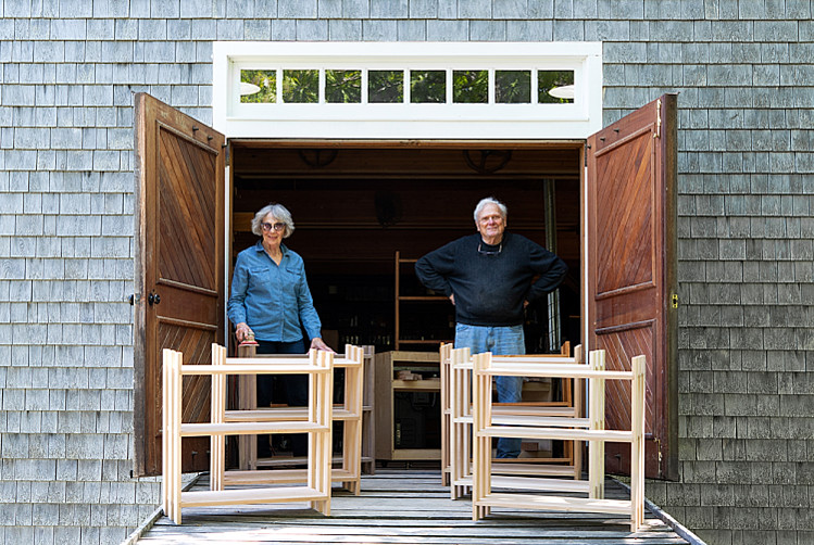 Mary Moser on left and Tom Moser on right stand in the doorway of his workshop behind bookshelves they built for their grandchildren
