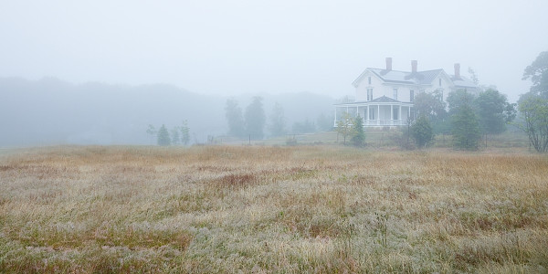Victorian home set back in a field with sparse trees on a foggy day