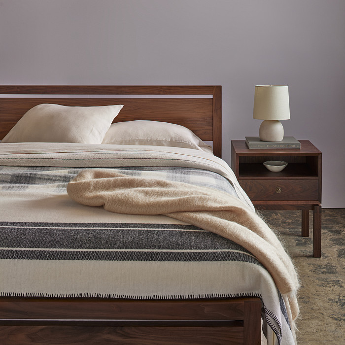 Walnut bed with woolen linens and walnut side table with brass knobs, book and white lamp