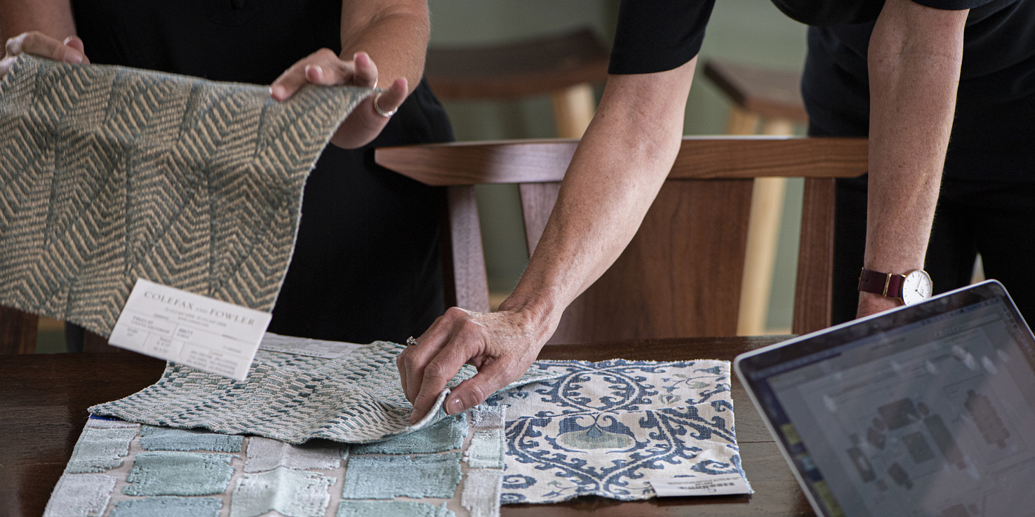 Hands touching upholstery samples on walnut table