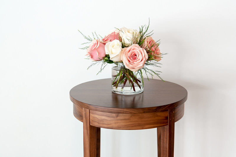 A bouquet of pink and white roses on a round minimus table in walnut.